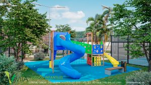 Vista de un colorido parque de juegos infantiles en un entorno tropical. El área cuenta con un suelo de caucho de seguridad azul y un gran módulo de juegos con toboganes (uno principal en espiral de color azul y otro más pequeño de color amarillo), escaleras y paneles interactivos en colores primarios. Hay una banca de descanso cercana, y el área está rodeada de árboles frondosos y palmeras. Al fondo se distingue una estructura de palapa y al lado derecho una cancha deportiva cercada. En la esquina se lee 'VITA JUEGOS INFANTILES' con información de contacto.