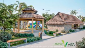 Vista de un kiosco o pabellón de madera con techo de palapa (paja), diseñado para reuniones y descanso al aire libre en un entorno ajardinado. El kiosco se ubica cerca de un camino pavimentado y está rodeado de césped y bancos de madera. A la derecha se ve una edificación rústica con muros de piedra y techo de palapa (posiblemente el restaurante). Al fondo se distingue la zona de juegos infantiles. En la parte inferior derecha se lee 'KIOSCO VITA RESIDENCIAL' con información de contacto.