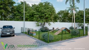 Vista de un área de juegos y entrenamiento para mascotas (dog park) dentro de un complejo residencial. El espacio está cercado con malla verde, cuenta con una superficie de césped, rampas de madera y obstáculos para perros. Se aprecian árboles frondosos, una banca de descanso, un bote de basura y un vehículo oscuro estacionado en el pavimento de adoquines adyacente. En la parte inferior se lee 'VITA RESIDENCIAL ÁREA DE MASCOTAS' con información de contacto.