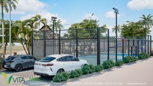 Vista de una moderna cancha de pádel de piso azul en un complejo residencial, rodeada por una cerca metálica negra. El área deportiva cuenta con iluminación nocturna y está ambientada con palmeras y vegetación tropical. Se aprecian dos vehículos de lujo (uno blanco y uno gris oscuro) estacionados en el área adyacente. Al fondo, se vislumbra un techo de palapa y una zona de juegos infantiles. En la esquina se lee 'VITA RESIDENCIAL PADEL' con información de contacto.